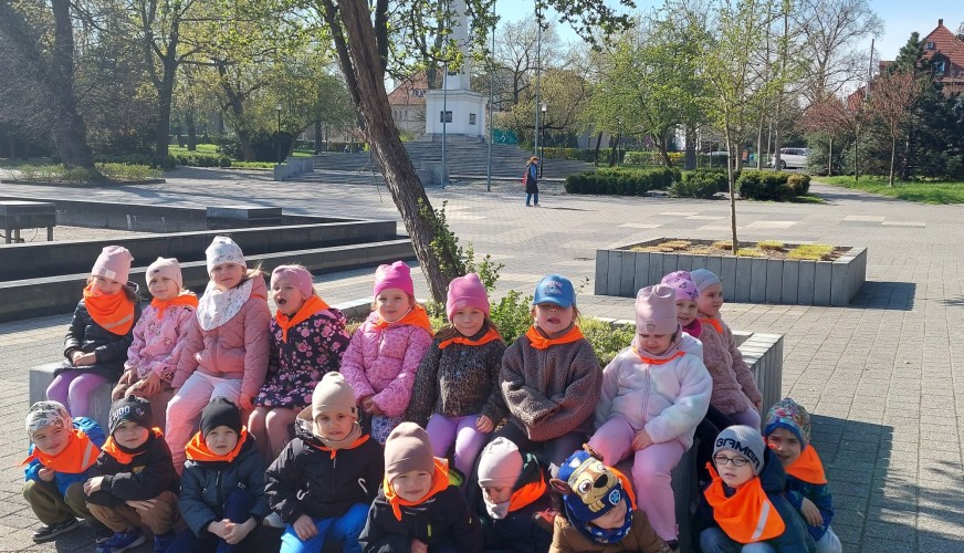 Grupa małych dzieci w pomarańczowych kamizelkach siedzi w Parku Słowiańskim